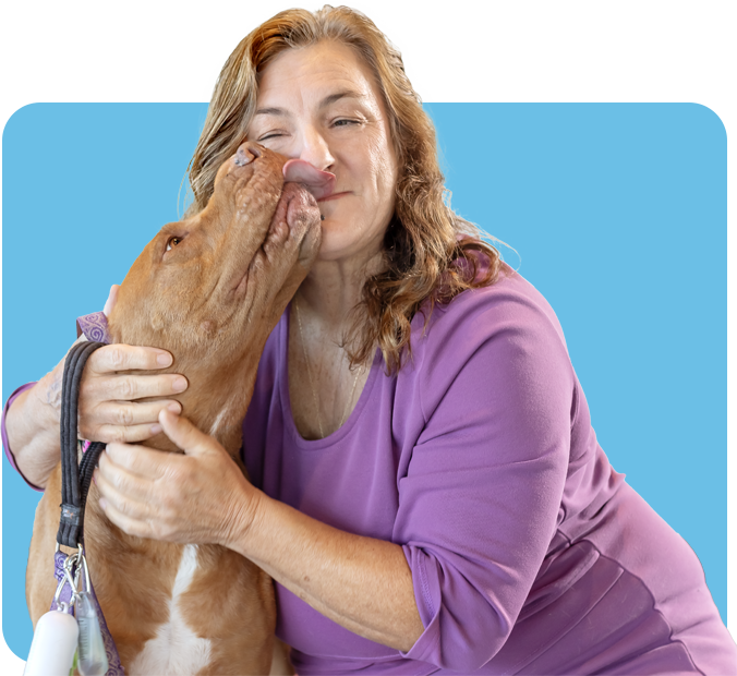 Barbra M. hugs her pitbull while grinning widely and getting licked by her dog